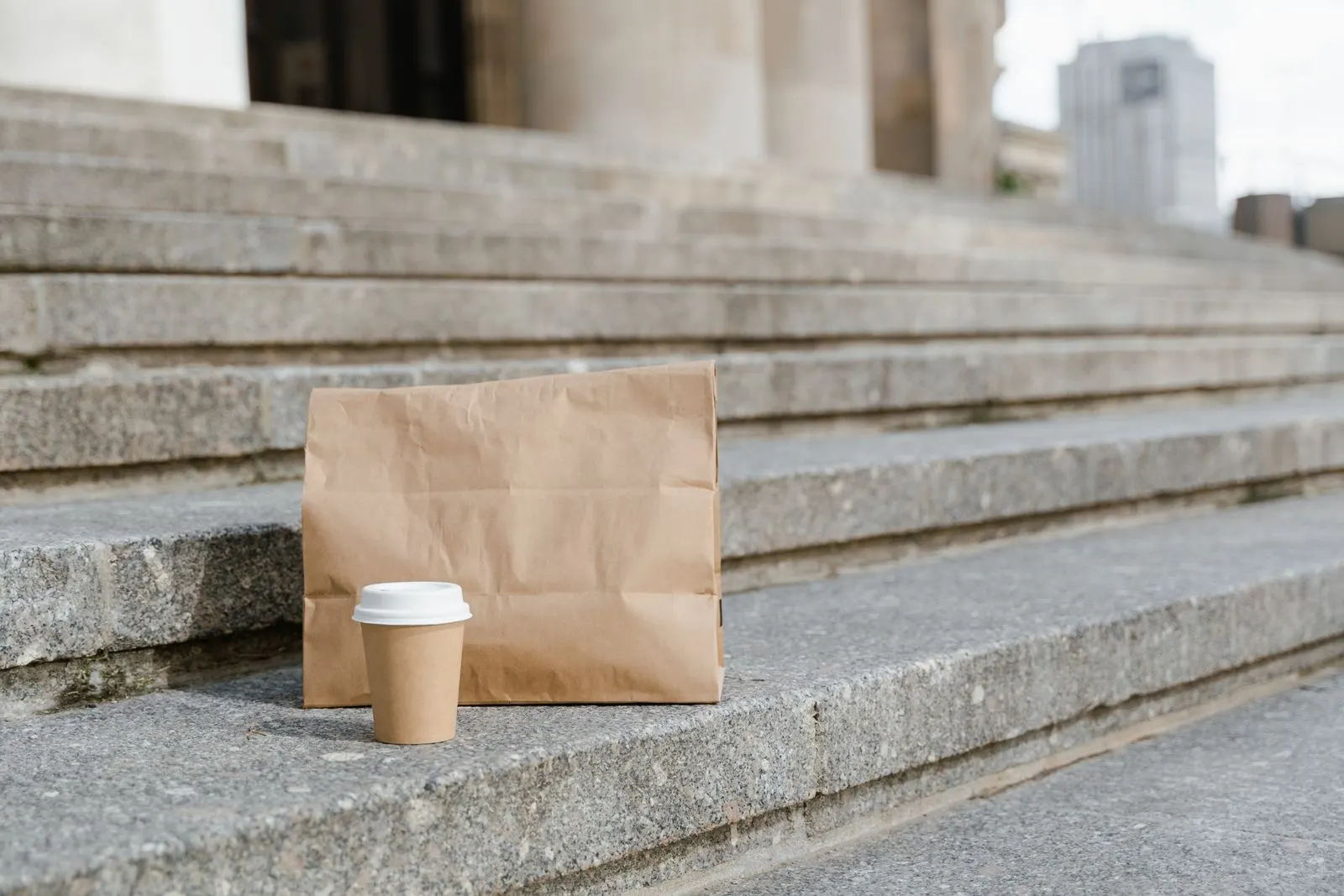 A brown paper bag and a takeaway coffee cup on stone steps