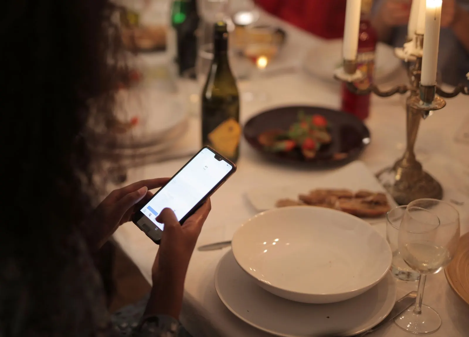 Une cliente consulte un menu sur son smartphone à une table de restaurant dressée aux chandelles