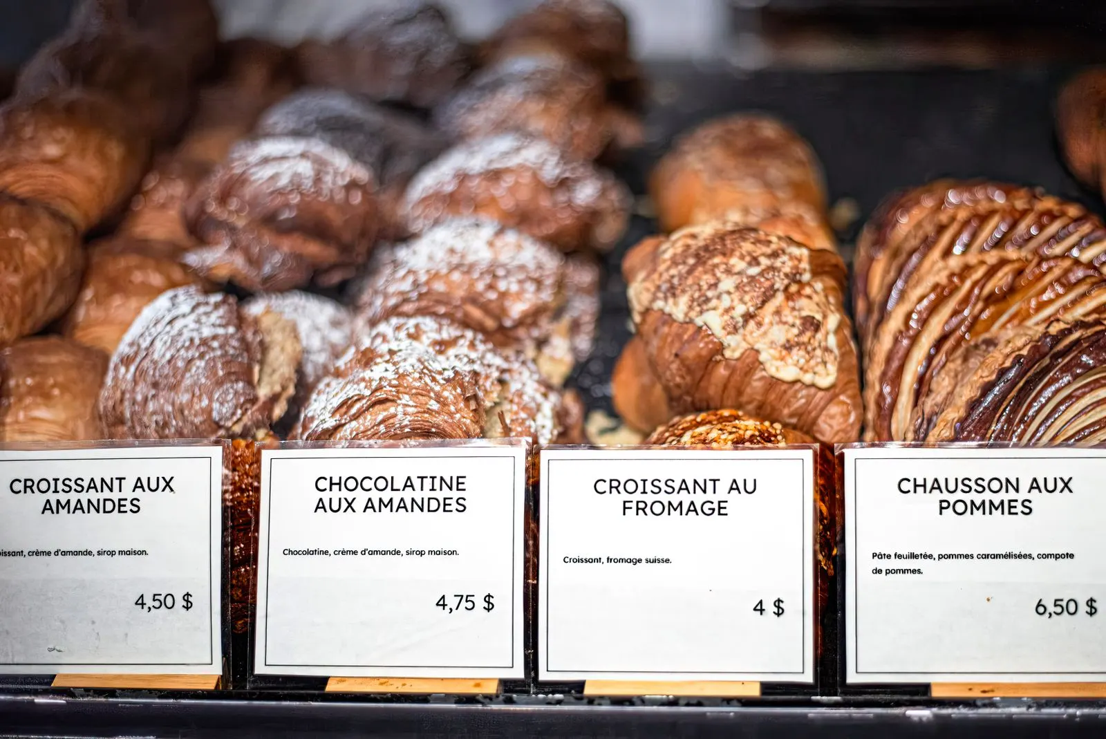 Een bakkerijvitrine met amandelcroissants, chocoladebroodjes en appelflappen, elk met een prijskaartje