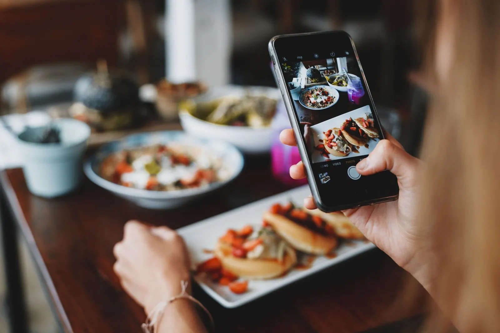 A guest photographs a plate of tacos on a restaurant table with her smartphone